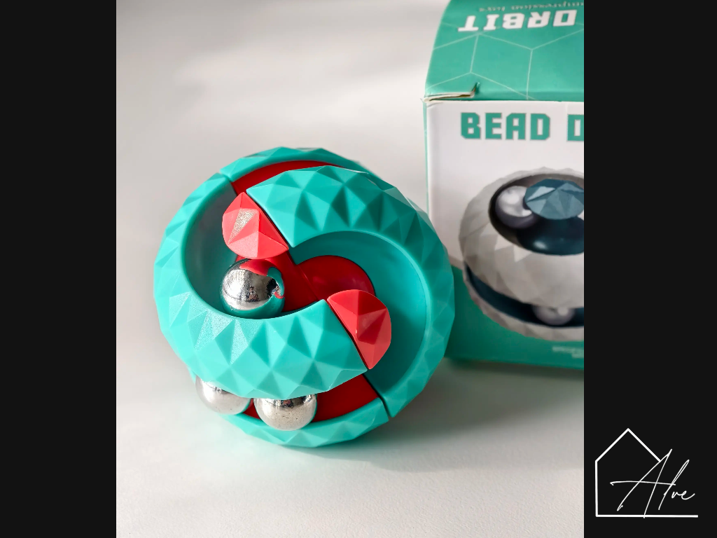 Teal and red sphere fidget ball beside its packaging box, steel beads visible inside